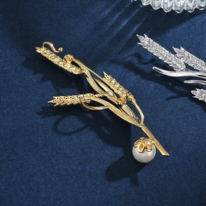 Élégante broche en épi de blé doré avec perle lustrée sur un fond de velours bleu marine