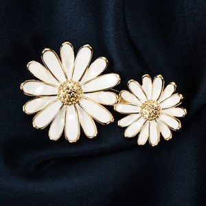 Broche marguerite élégante en émail blanc et métal doré sur fond de soie bleu marine