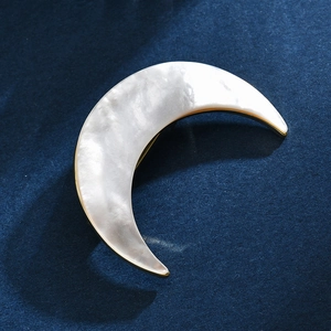 Elegant crescent moon brooch with white sea shell inlay and golden trim on navy blue fabric