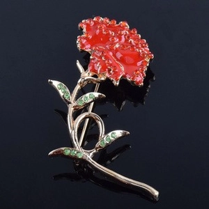 Elegant red carnation brooch with rhinestones and gold stem on a black mirror background