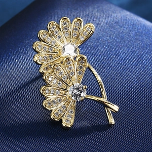 Close-up of golden flower brooch with sparkling zircon petals on blue silk fabric