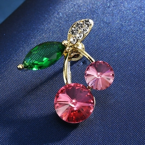 Macro shot of cherry-shaped brooch featuring pink crystals and green leaf on blue fabric