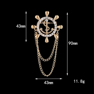 Golden nautical rudder brooch with white rhinestones and dangling chains on black background