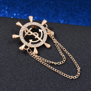 Macro detail of golden nautical ship wheel brooch with dollar sign anchor and metal chains
