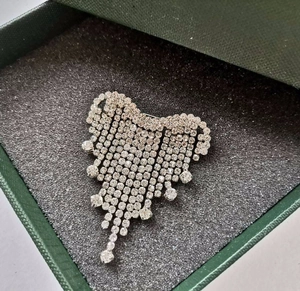 Makroaufnahme der funkelnden Herz-Strass-Brosche mit Quasten in einer grünen Geschenkbox