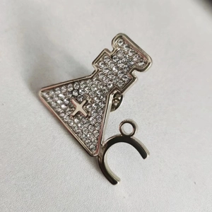Macro detail of silver conical flask brooch with white crystals and cross symbol