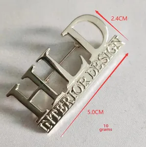 Detailed view of golden metal letter brooch with dimensions 5.0cm and 2.4cm on grey background