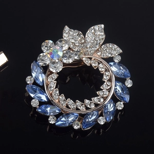 Close-up of a floral round brooch featuring iridescent gems and navy marquise crystals