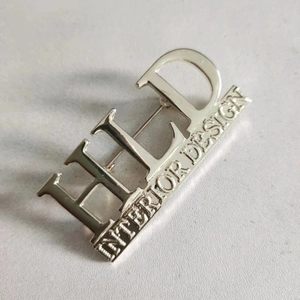 Polished silver metal brooch with HID Interior Design lettering for coat accessories