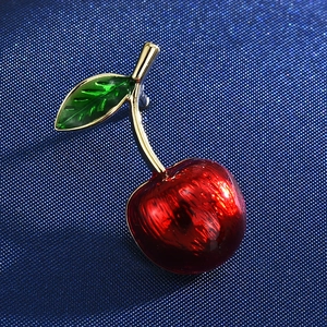 Detailed macro shot of a cherry brooch featuring red glossy fruit and green leaves