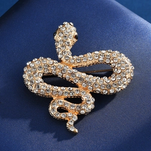 Détail macro d'une broche serpent dorée avec cristaux blancs étincelants sur soie bleue