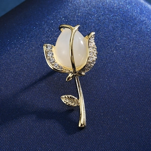 Macro detail of a gold rose brooch featuring an opal stone and sparkling zircon accents