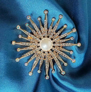 Broche soleil élégante avec perle et cristaux sur un fond de soie vert foncé