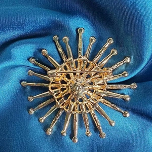 Broche tournesol dorée vue de dos avec épingle de sûreté sur fond de soie bleu foncé