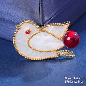 Macro detail of bird brooch with white shell, red crystal eyes and gold bead trim