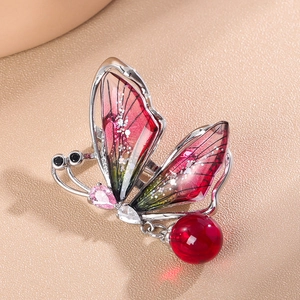 Vue détaillée de broche papillon aux ailes colorées et perle rouge délicate pendante