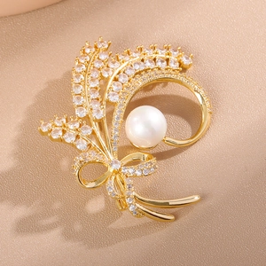 Macro shot of gold wheat brooch with sparkling zircons, bow detail and white pearl