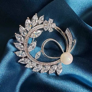 Close-up of luxury leaf brooch with marquise zircons and white pearl on navy silk