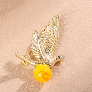 Elegant gold bird brooch with white enamel wings and a large amber marble bead