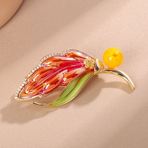 Macro shot of leaf brooch with red enamel gradient, golden rose and zircon accents