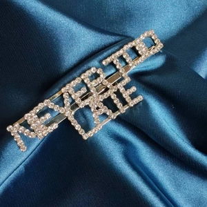 Broche dorée NEVER TOO LATE ornée de strass sur un fond de soie bleu foncé luxueux