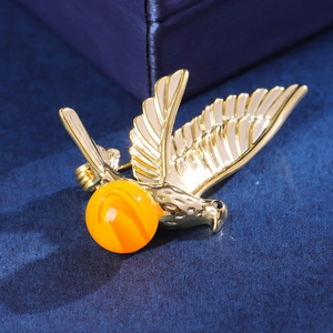 Elegant gold bird brooch with amber bead, featuring detailed feather texture and crystal eyes