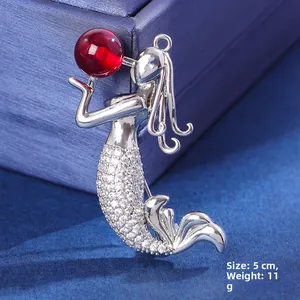Macro detail of mermaid brooch with silver metal, white zircons and red crystal bead