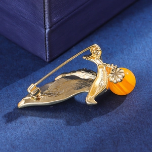 Detailed back view of golden bird brooch with orange amber bead on blue velvet