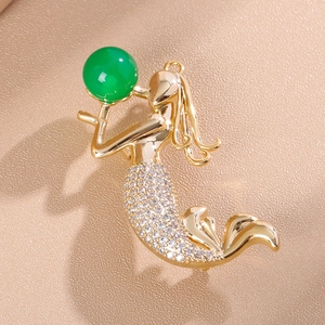 Vue détaillée d'une broche sirène dorée avec perle verte et accents en zircone cubique
