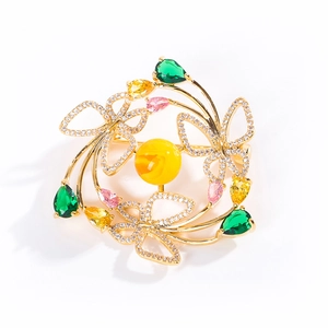 Broche couronne papillon dorée avec perle et cristaux colorés sur un fond blanc pur