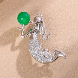 Détail macro d'une broche sirène argentée avec pierre verte et zircons brillants