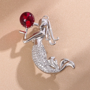 Vue macro d'une broche sirène avec pierre rouge et zircons pavés sur métal argenté