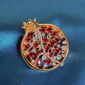 Nahaufnahme der Granatapfel-Brosche mit roten Zirkoniasteinen auf dunkelblauem Seidenstoff