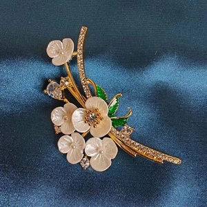 Detailed macro view of white enamel flower brooch with gold leaves and crystal accents