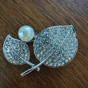Elegante spilla a forma di foglia con metallo argento, strass scintillanti e perla bianca