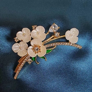 Elegant flower brooch with white enamel petals and pearl center on dark blue silk background