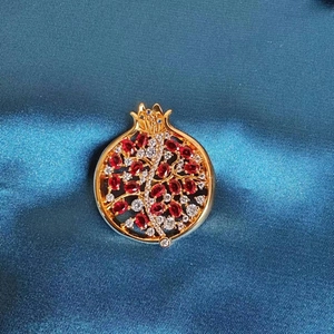 Eleganter Granatapfel Brosche mit roten Zirkonsteinen auf blauem Satinhintergrund