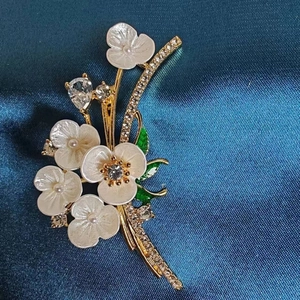 Elegant gold flower brooch with white petals, emerald leaves and crystal accents