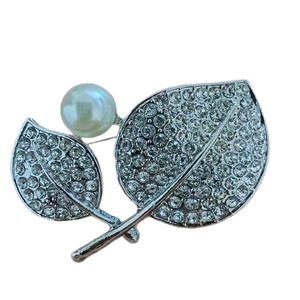 Elegante spilla a foglia argento con micro cristalli e perla bianca su sfondo bianco