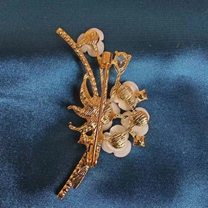 Macro detail of gold flower brooch back featuring secure pin and white camellia design