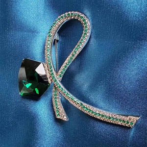 Macro shot of R-shaped ribbon brooch with emerald green square stone and micro-pave crystals