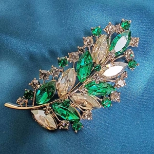 Elegant emerald and champagne crystal leaf brooch on a luxurious satin background