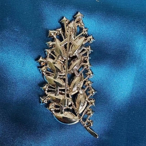Elegant golden leaf brooch with detailed back clasp on a blue satin background