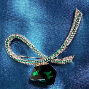 Elegant ribbon brooch featuring emerald green crystals and a large dark green gemstone