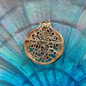 Rückansicht der goldenen Granatapfel-Brosche mit roten Zirkonia-Samen auf Blau