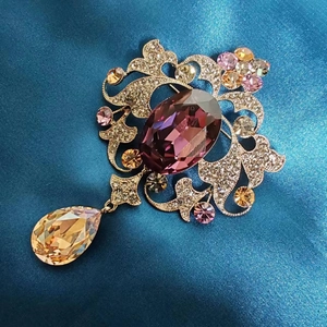 Dettaglio macro della spilla vintage con cristallo viola e pendente a goccia champagne