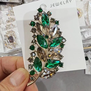 Elegant leaf-shaped brooch with green and gray crystals on a gold-plated base