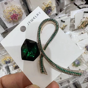 Detailed macro view of a ribbon bow brooch featuring a large green gemstone and crystals