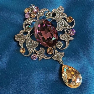 Dettaglio di spilla a fiore vintage con cristallo viola e pendente a goccia champagne