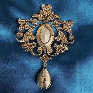 Spilla dorata vintage con ciondolo a goccia e spilla di sicurezza su raso blu scuro
